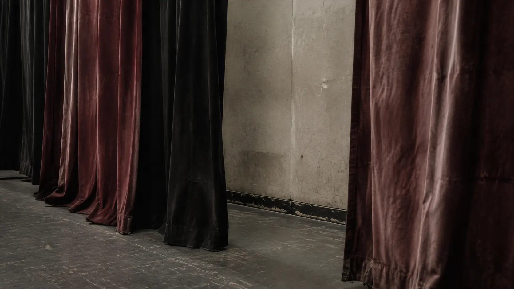 Heavy curtains hang at irregular depths beside a scuffed backstage wall.